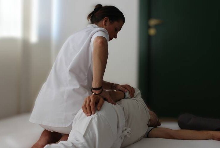 Operatrice in camice bianco che preme con le mani la schiena di una persona sdraiata, in una stanza luminosa.