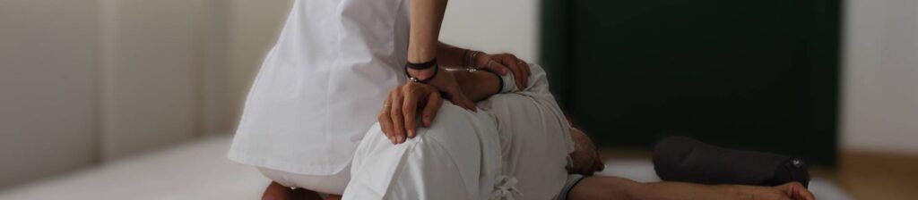 Mani di un'operatrice appoggiate sulla schiena di una persona sdraiata, in una stanza luminosa.